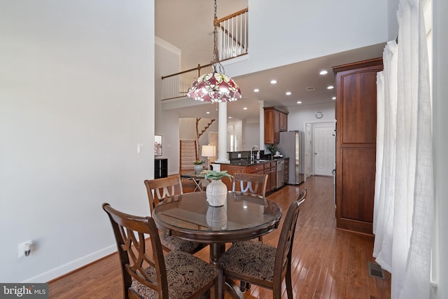 dining room featuring visible vents, a towering ceiling, stairway, baseboards, and wood-type flooring