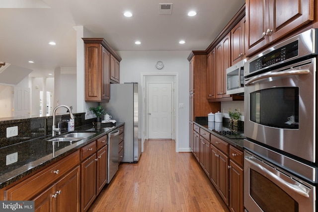 kitchen featuring visible vents, dark stone counters, a sink, light wood finished floors, and appliances with stainless steel finishes