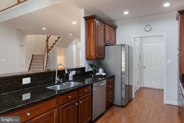 kitchen featuring baseboards, light wood-type flooring, a sink, dark stone countertops, and stainless steel appliances