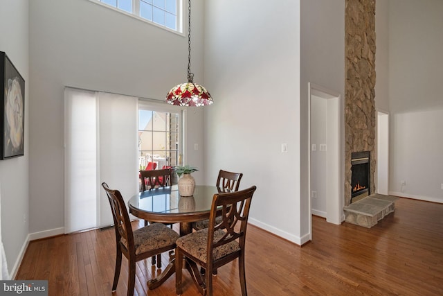 dining space with a fireplace, baseboards, wood finished floors, and a towering ceiling