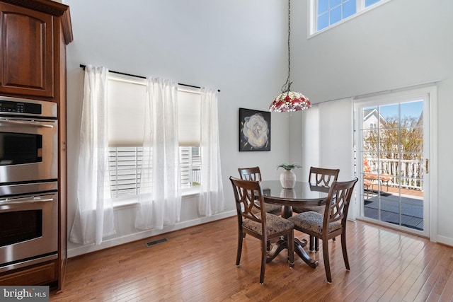 dining area with visible vents, wood-type flooring, a towering ceiling, and baseboards