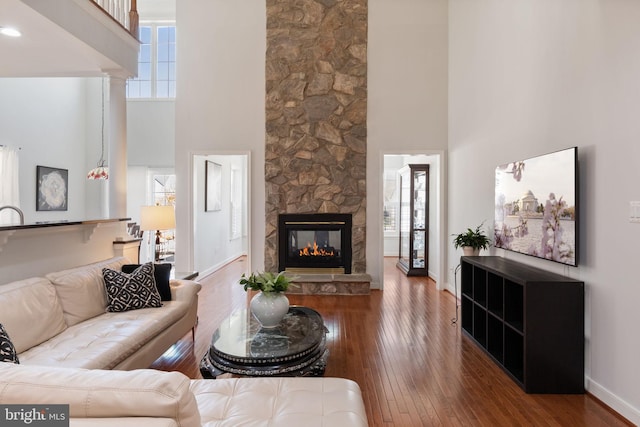 living room with a fireplace, a wealth of natural light, wood-type flooring, and a towering ceiling
