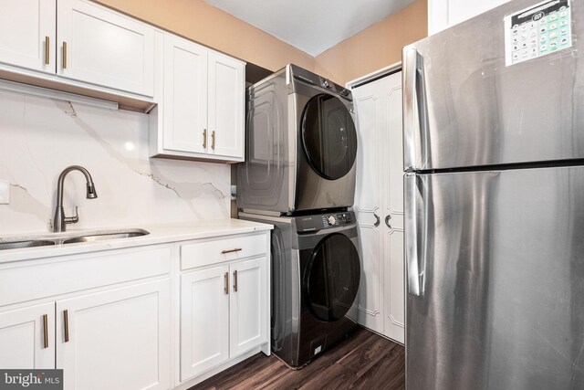 clothes washing area featuring a sink, stacked washer / dryer, and dark wood finished floors