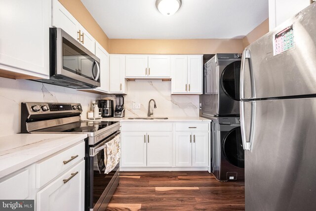 kitchen with stacked washer and clothes dryer, white cabinets, a sink, dark wood finished floors, and stainless steel appliances