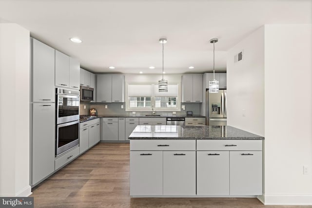 kitchen featuring decorative light fixtures, appliances with stainless steel finishes, a sink, dark stone countertops, and light wood finished floors