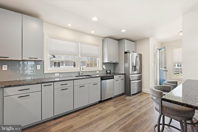 kitchen featuring appliances with stainless steel finishes, a sink, light wood finished floors, dark stone counters, and recessed lighting
