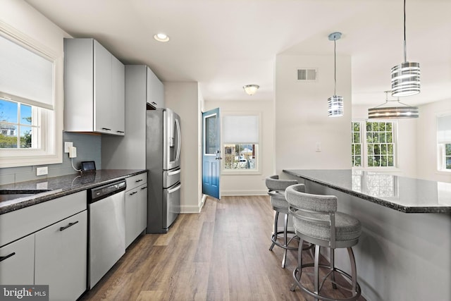 kitchen with a kitchen bar, visible vents, appliances with stainless steel finishes, wood finished floors, and dark stone countertops