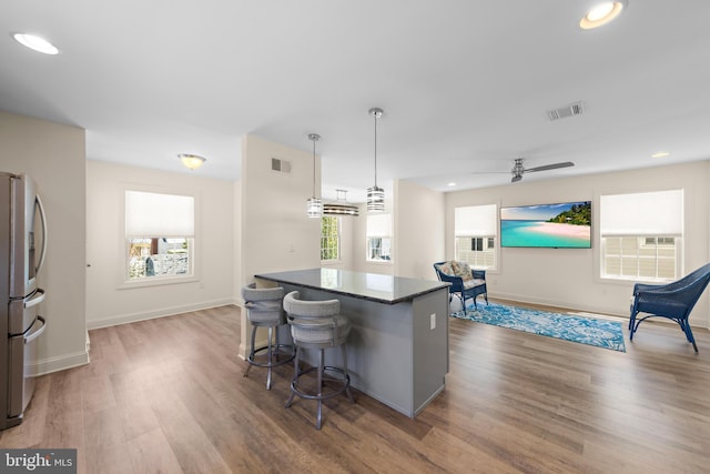 kitchen with stainless steel refrigerator with ice dispenser, wood finished floors, visible vents, and a breakfast bar