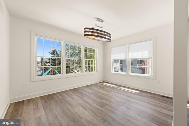 unfurnished dining area featuring a chandelier, visible vents, a wealth of natural light, and wood finished floors