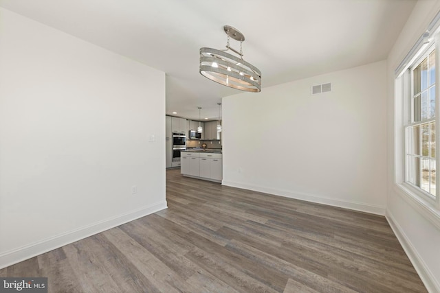 unfurnished dining area with visible vents, dark wood finished floors, baseboards, and a notable chandelier