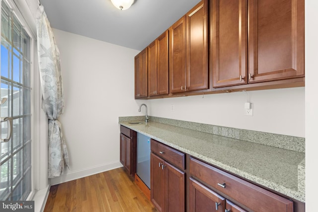 kitchen featuring baseboards, light stone counters, a sink, and light wood finished floors