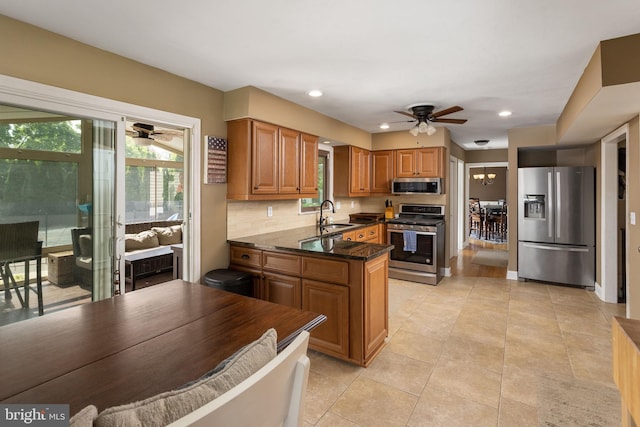 kitchen featuring brown cabinetry, ceiling fan, a sink, a peninsula, and appliances with stainless steel finishes