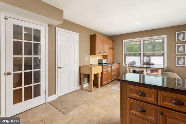 kitchen featuring brown cabinets, dark stone countertops, visible vents, light tile patterned flooring, and recessed lighting