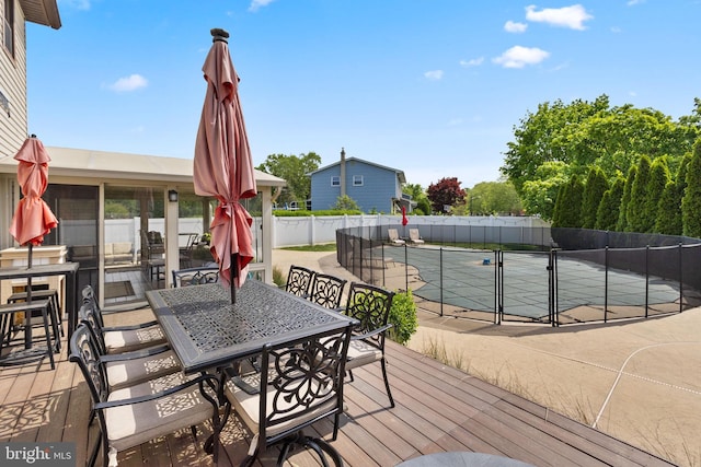 wooden terrace featuring a tennis court, outdoor dining area, and fence