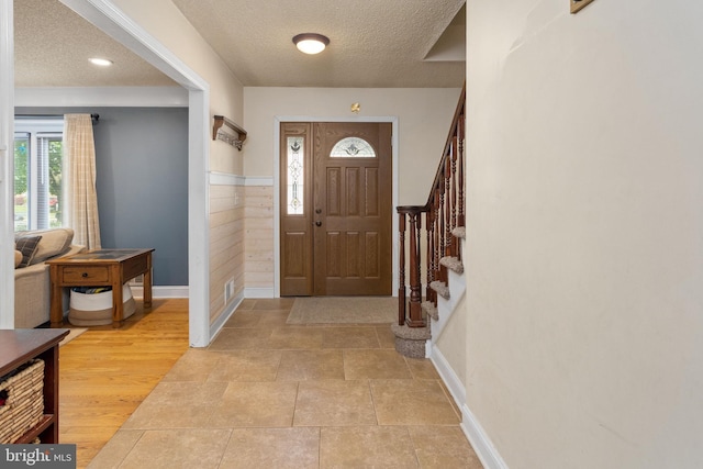 entrance foyer featuring a textured ceiling, stairs, baseboards, and a wainscoted wall