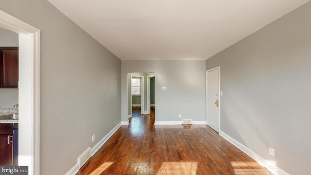 empty room with visible vents, a sink, dark wood-style flooring, and baseboards