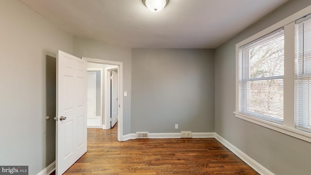 spare room featuring baseboards, visible vents, a wealth of natural light, and dark wood finished floors