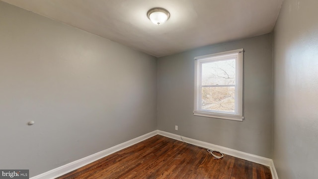 spare room featuring baseboards and dark wood finished floors