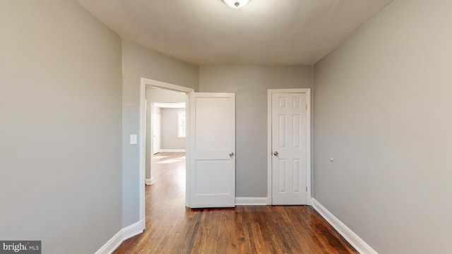 corridor featuring baseboards and dark wood-type flooring