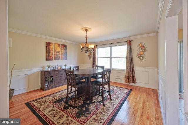 dining area with crown molding, a notable chandelier, light wood-type flooring, and a wainscoted wall