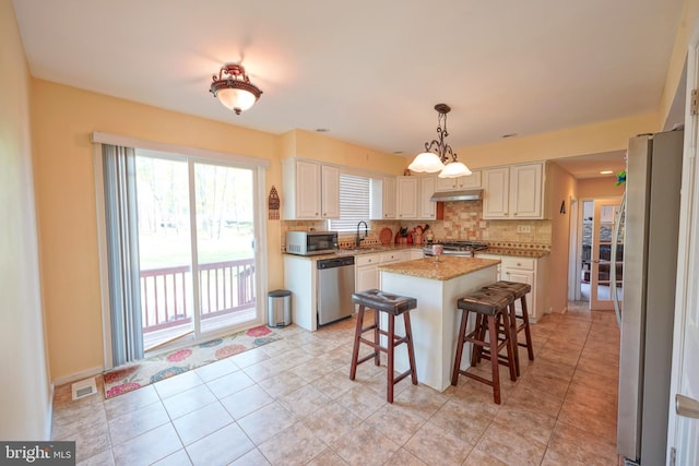 kitchen featuring appliances with stainless steel finishes, a sink, tasteful backsplash, under cabinet range hood, and visible vents