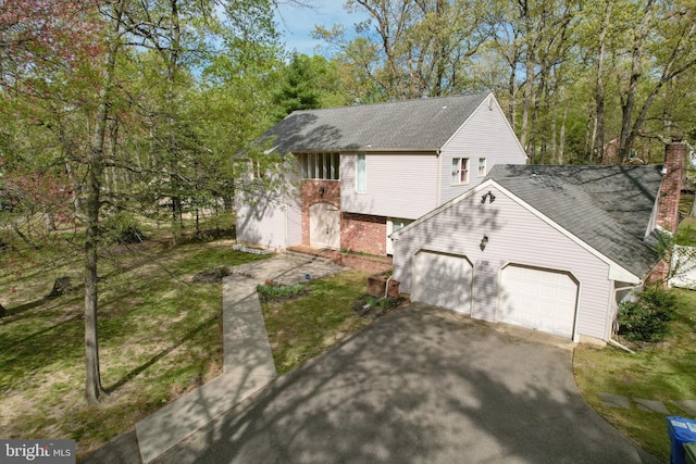 view of home's exterior featuring driveway, a chimney, a lawn, an attached garage, and a shingled roof
