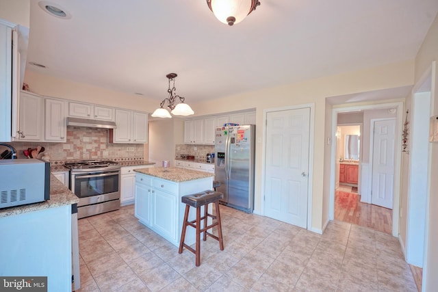 kitchen with decorative backsplash, appliances with stainless steel finishes, a center island, light stone counters, and white cabinets
