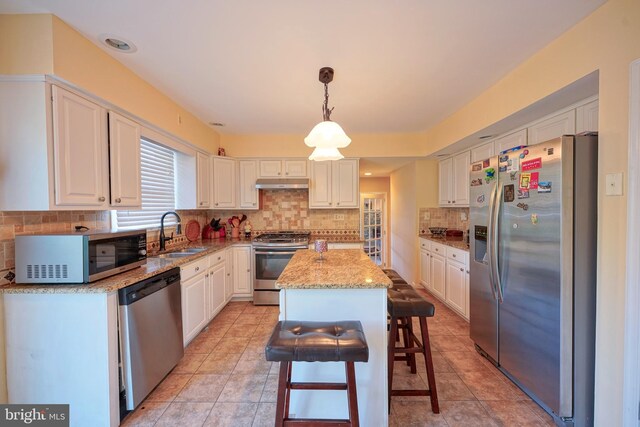kitchen featuring decorative backsplash, appliances with stainless steel finishes, light stone countertops, a sink, and under cabinet range hood