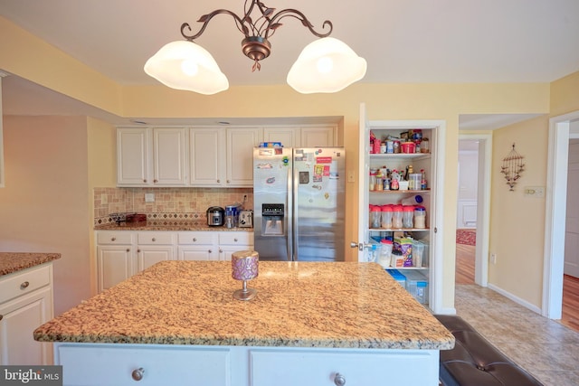 kitchen with stainless steel fridge, white cabinetry, backsplash, and light stone countertops