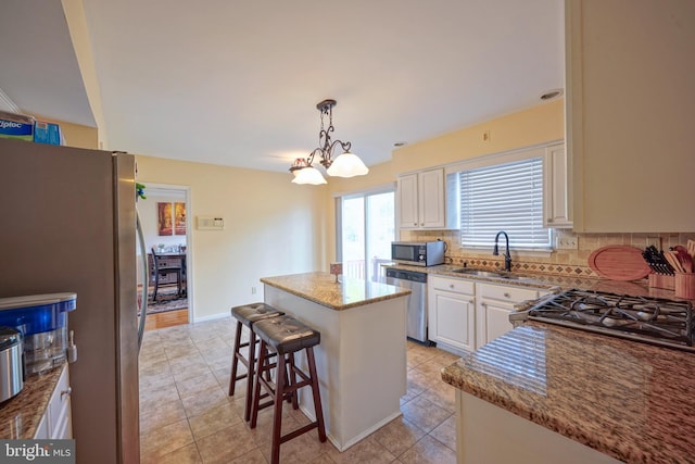 kitchen with appliances with stainless steel finishes, light stone counters, a sink, light tile patterned floors, and a kitchen island