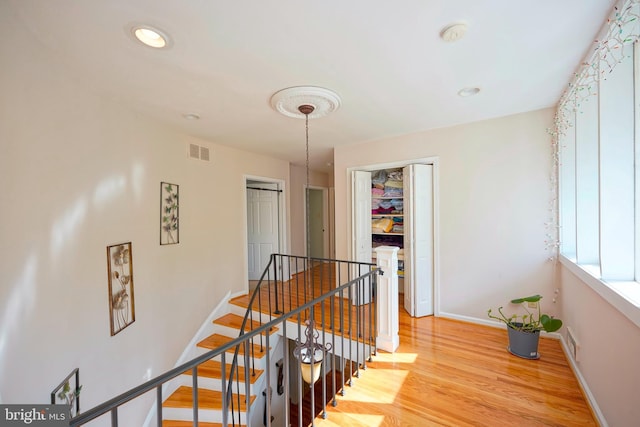 hallway featuring visible vents, wood finished floors, baseboards, an upstairs landing, and recessed lighting