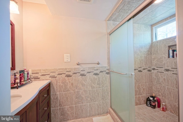 full bath with visible vents, tile walls, a stall shower, vanity, and a wainscoted wall