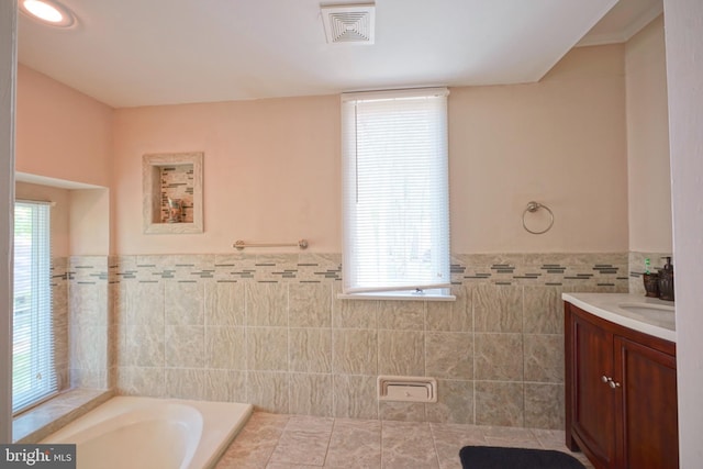 bathroom with visible vents, vanity, wainscoting, tile walls, and a bath