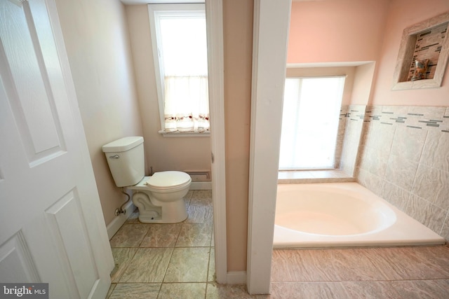 bathroom featuring a healthy amount of sunlight, baseboards, a garden tub, and toilet