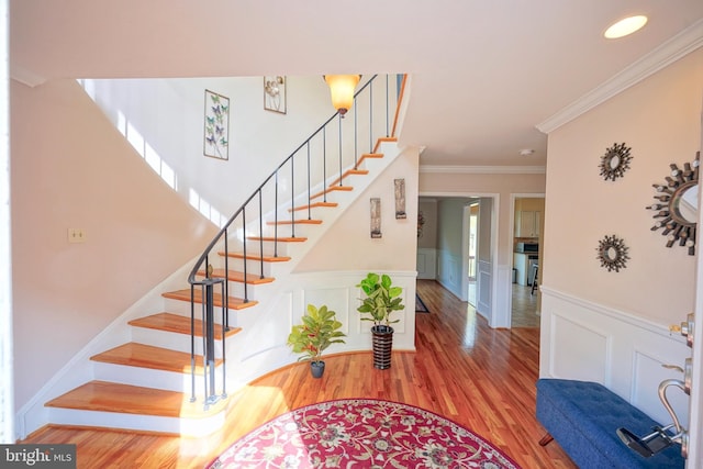 entryway with crown molding, wainscoting, a decorative wall, wood finished floors, and stairway