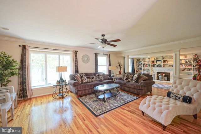 living room with a fireplace with raised hearth, ceiling fan, ornamental molding, and wood finished floors