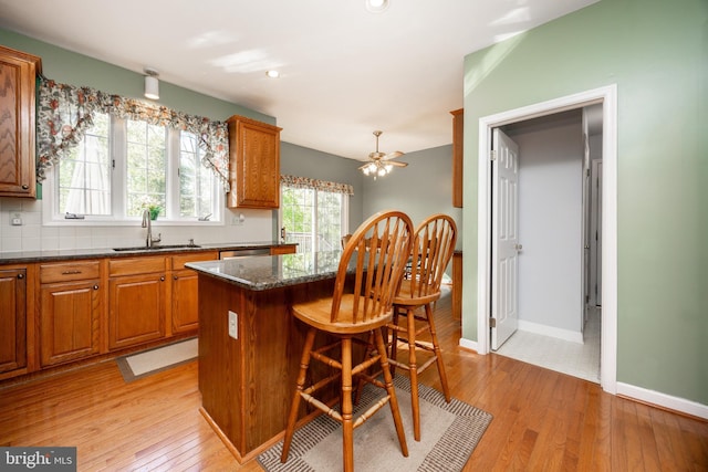 kitchen featuring a kitchen island, a breakfast bar, light wood-type flooring, brown cabinets, and a sink