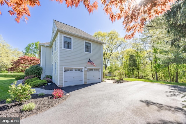 view of side of property with an attached garage, roof with shingles, and driveway