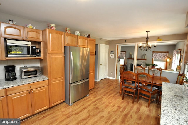 kitchen featuring an inviting chandelier, a toaster, light wood-style flooring, appliances with stainless steel finishes, and decorative light fixtures