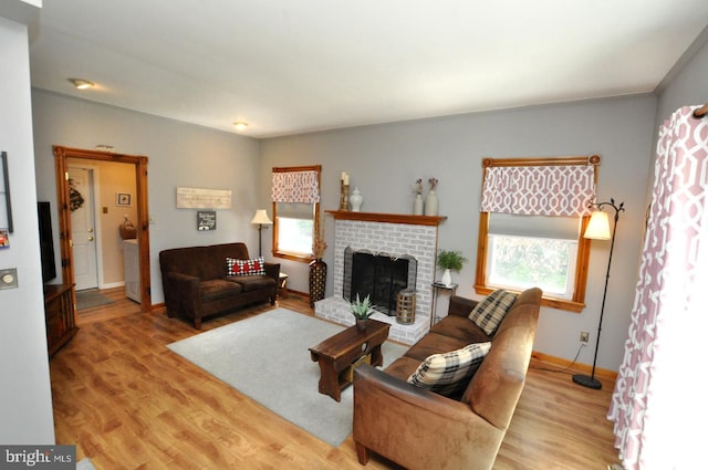 living room with a brick fireplace, baseboards, and light wood-type flooring