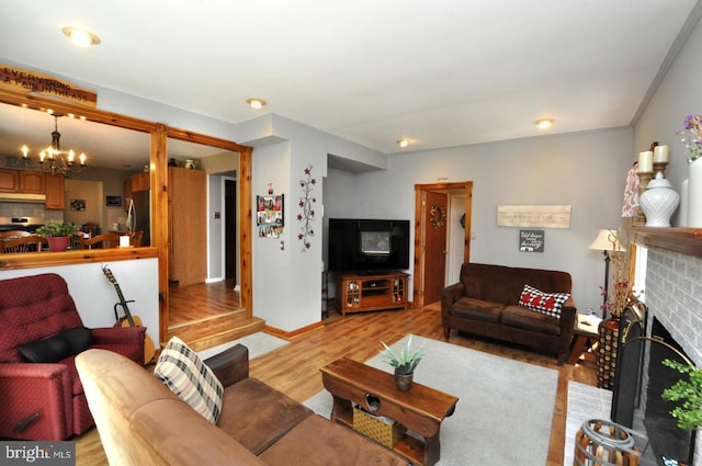 living room featuring light wood-style floors, an inviting chandelier, baseboards, and a fireplace