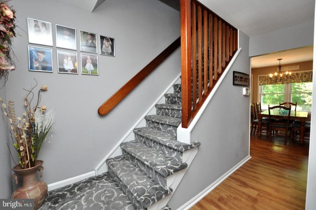 stairs featuring baseboards, wood finished floors, and a chandelier