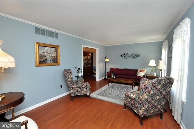living area with crown molding, visible vents, and wood finished floors