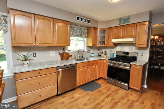 kitchen featuring light stone counters, a sink, appliances with stainless steel finishes, and under cabinet range hood