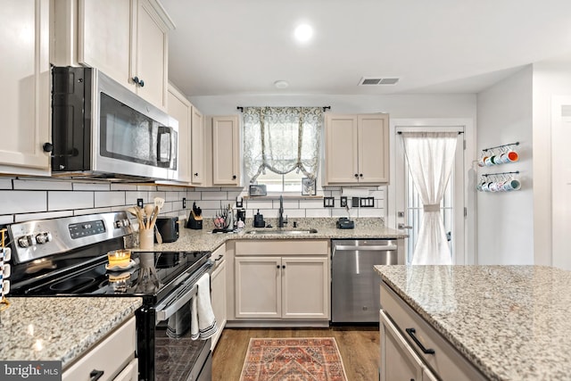 kitchen featuring visible vents, appliances with stainless steel finishes, light stone countertops, wood finished floors, and a sink