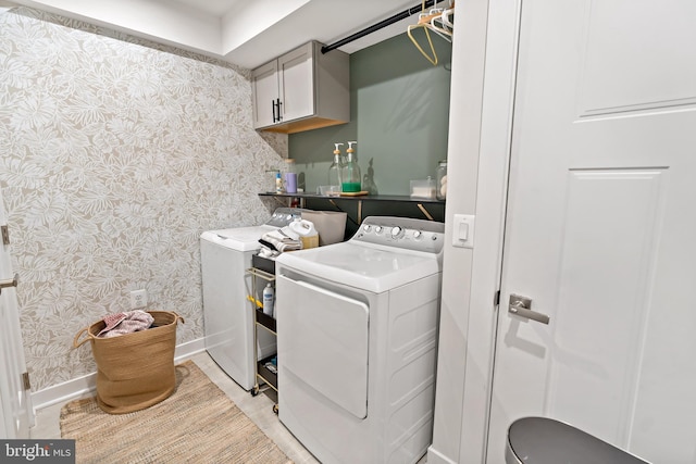 clothes washing area featuring baseboards, washer and clothes dryer, cabinet space, and wallpapered walls