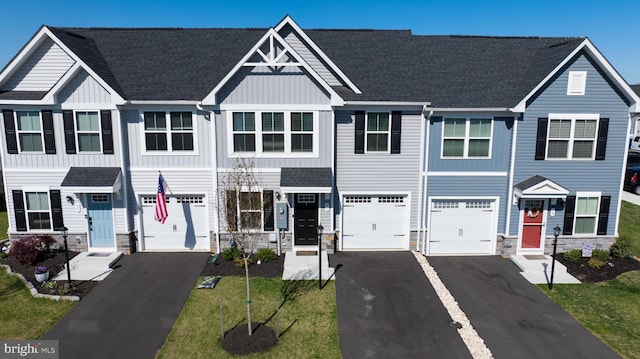 townhome / multi-family property with a garage, board and batten siding, aphalt driveway, and stone siding