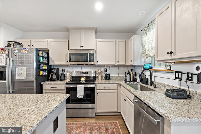 kitchen with backsplash, wood finished floors, a sink, white cabinets, and stainless steel appliances