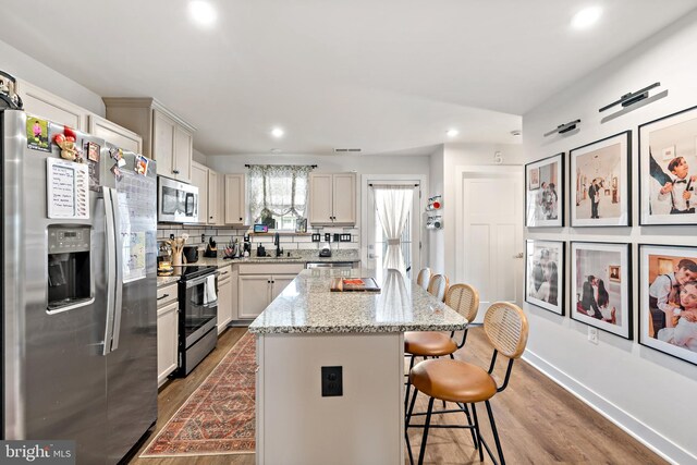 kitchen featuring a center island, stainless steel appliances, recessed lighting, wood finished floors, and a kitchen bar