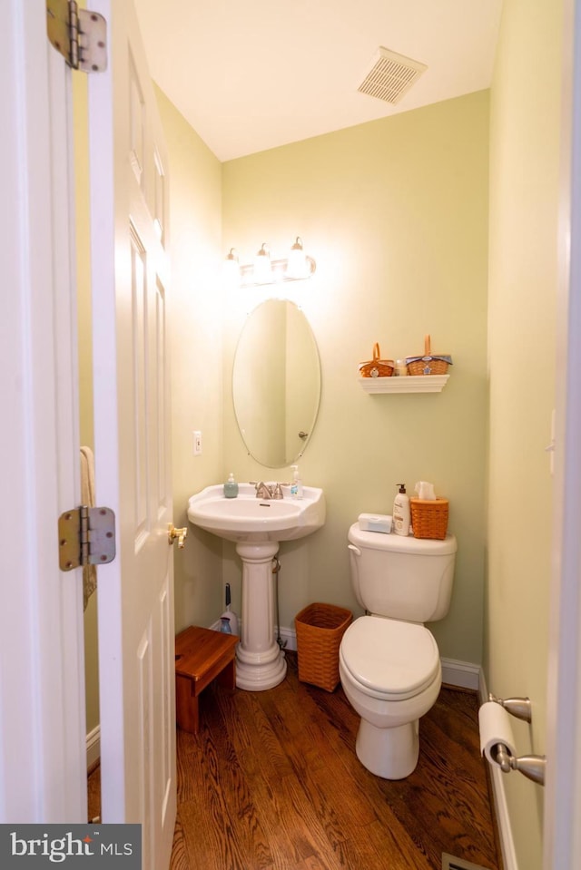 half bathroom with visible vents, wood finished floors, toilet, baseboards, and a sink